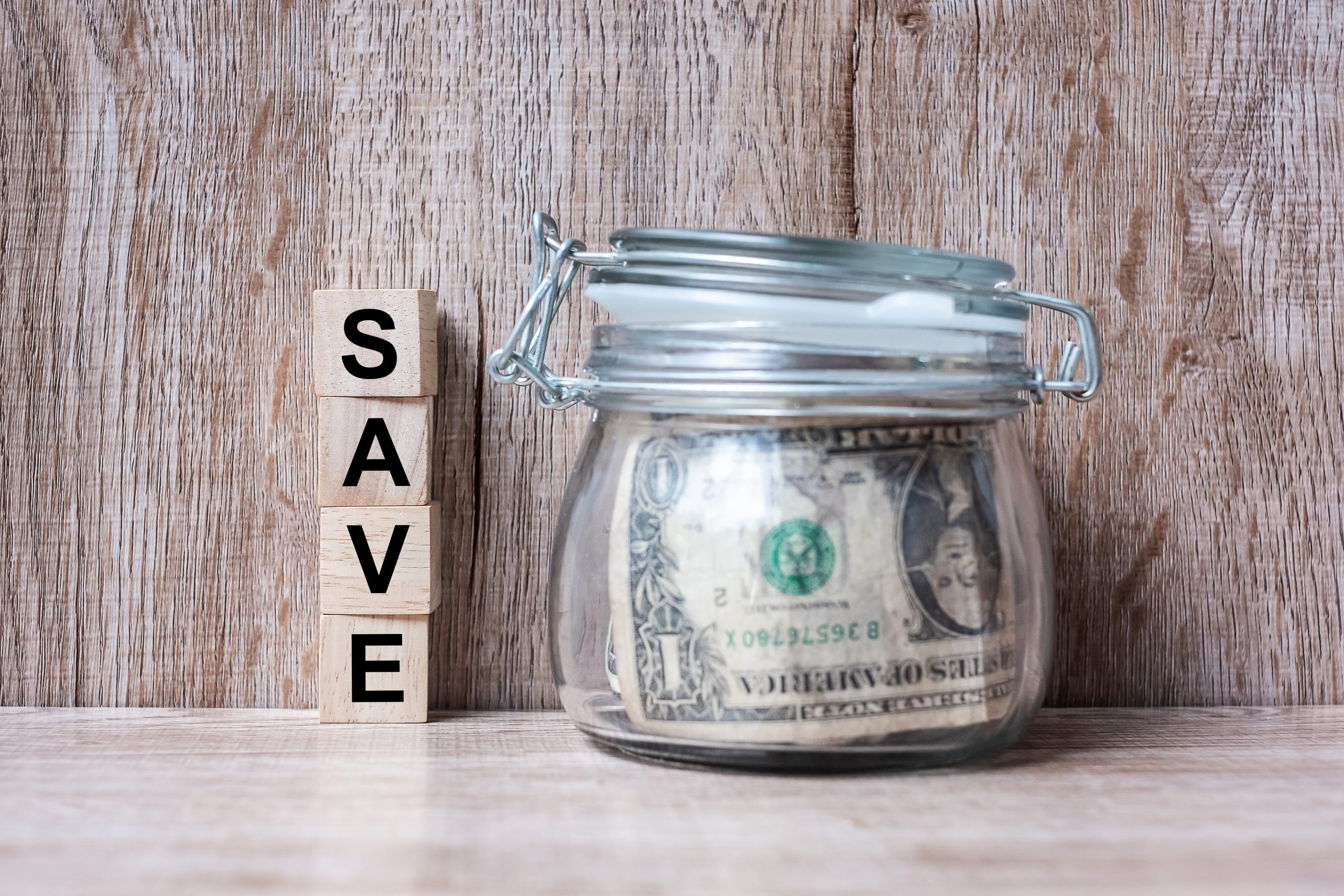 Wood block with SAVE text and American dollar money in glass jar. world saving day, business, investment, retirement planning, finance concept